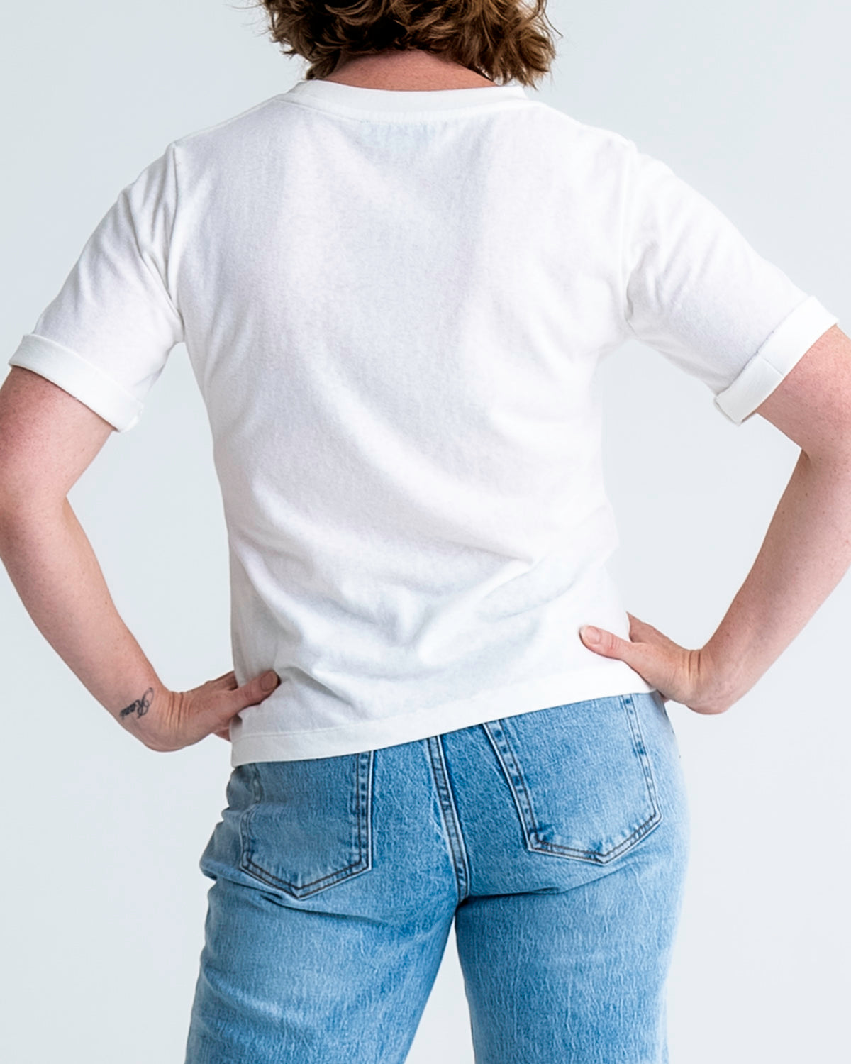 Back view of slim fit t-shirt in white, shown untucked, worn with jeans. T-shirt finishes mid-hip. Model wears size 8.