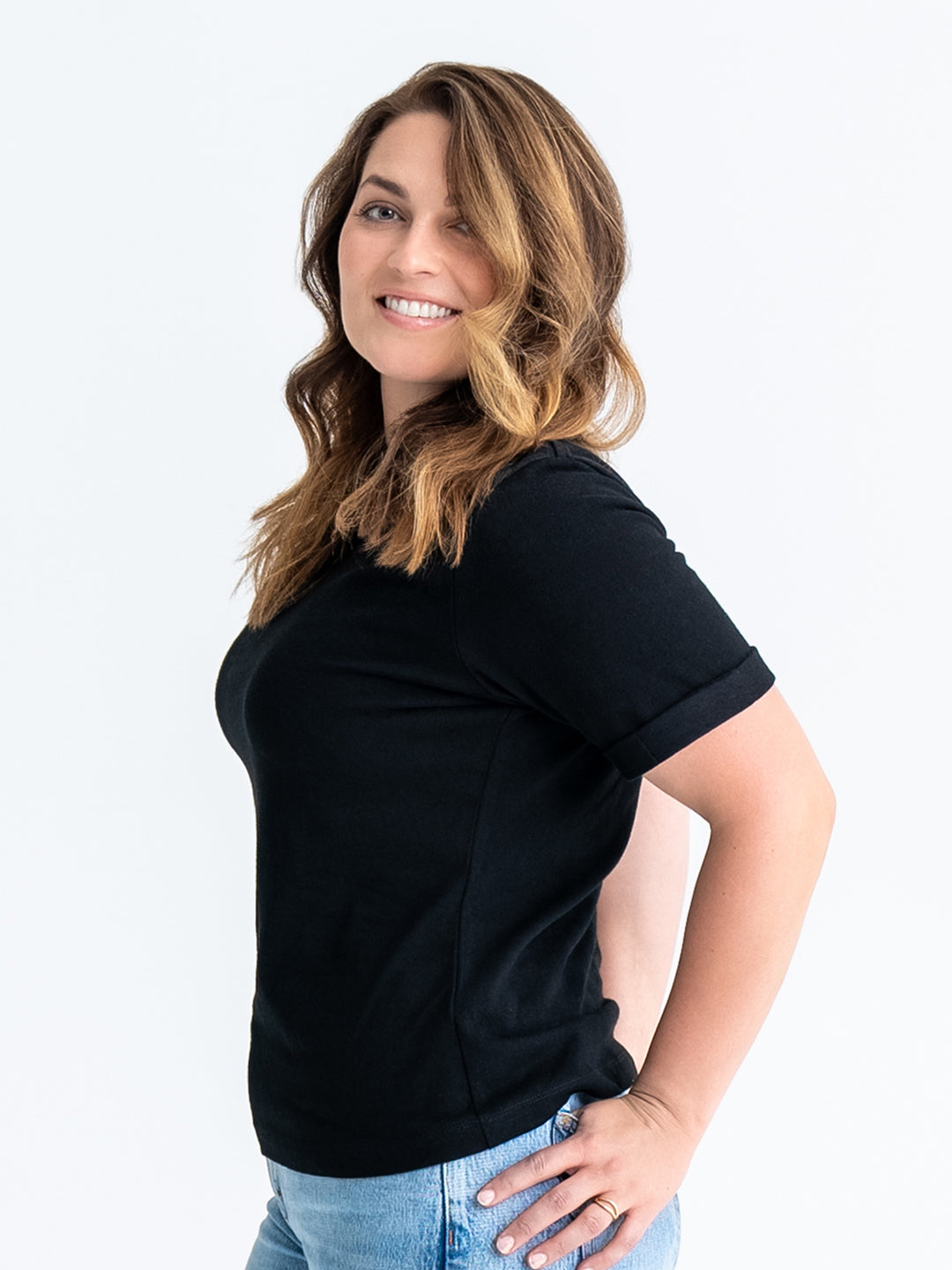 Side view of black t-shirt made for big boobs, shown untucked, finishes mid-hip. Model wears size 12.