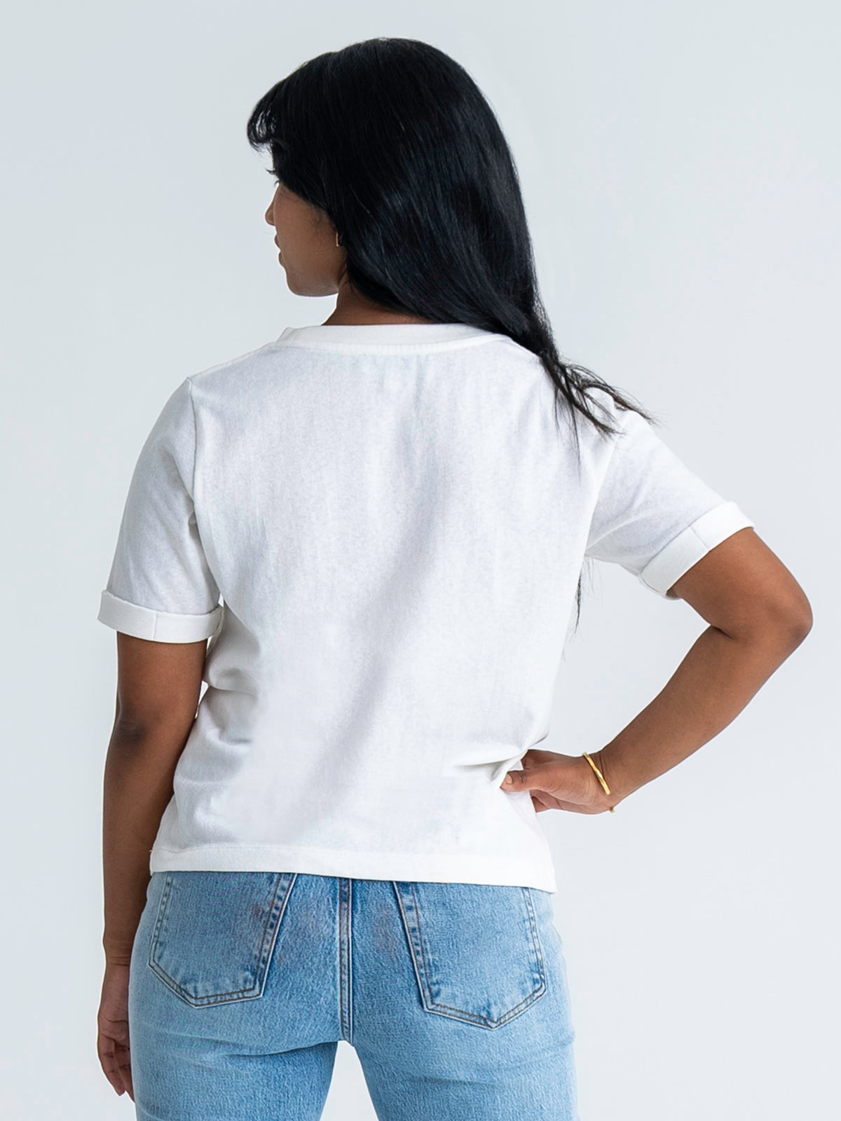 Back view of relaxed fit t-shirt in white, shown untucked, worn with jeans. T-shirt finishes mid-hip. Model wears size 8.