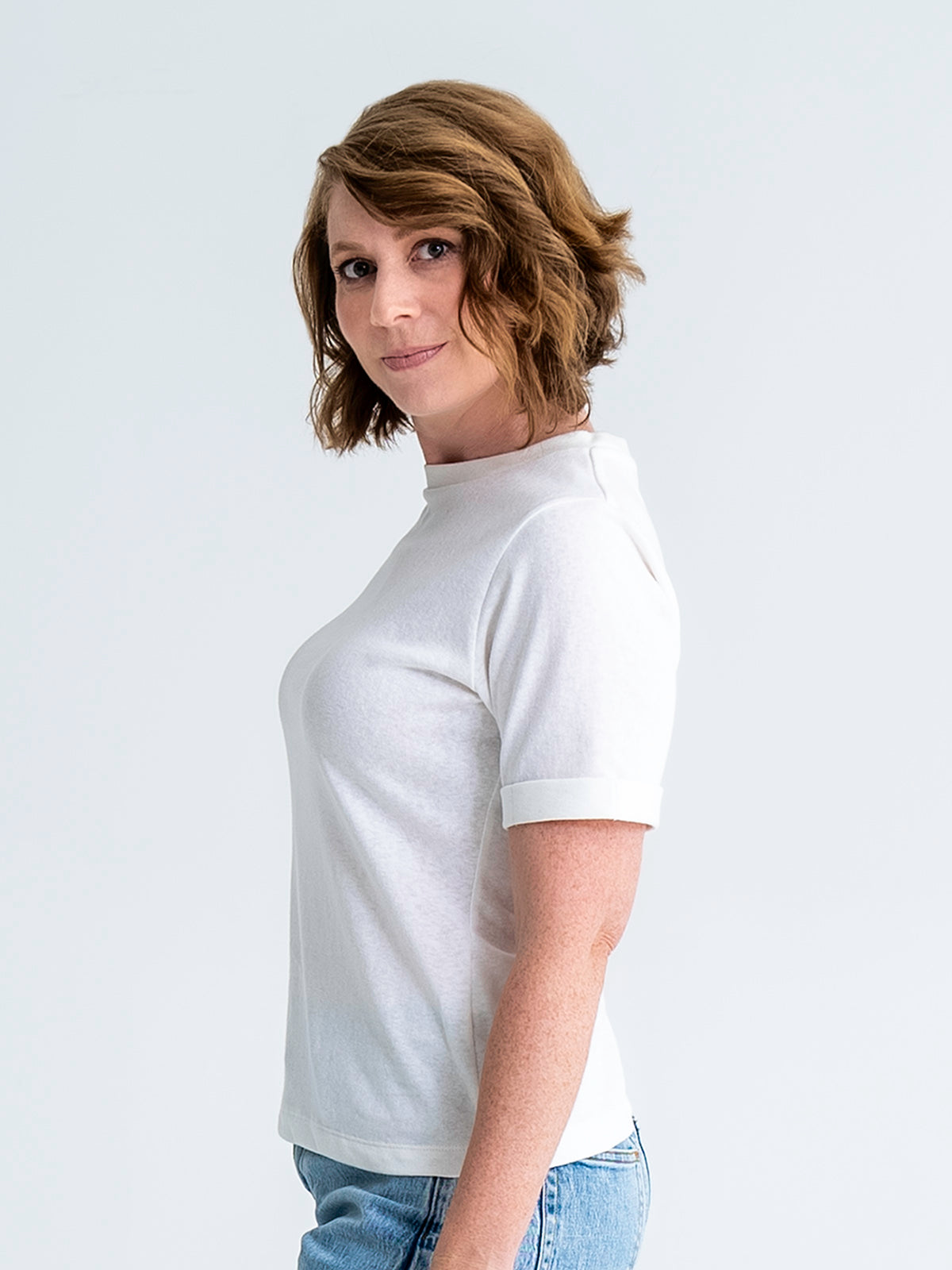 Side view of slim fit t-shirt in white, shown untucked, worn with jeans. T-shirt finishes mid-hip. Model wears size 8.