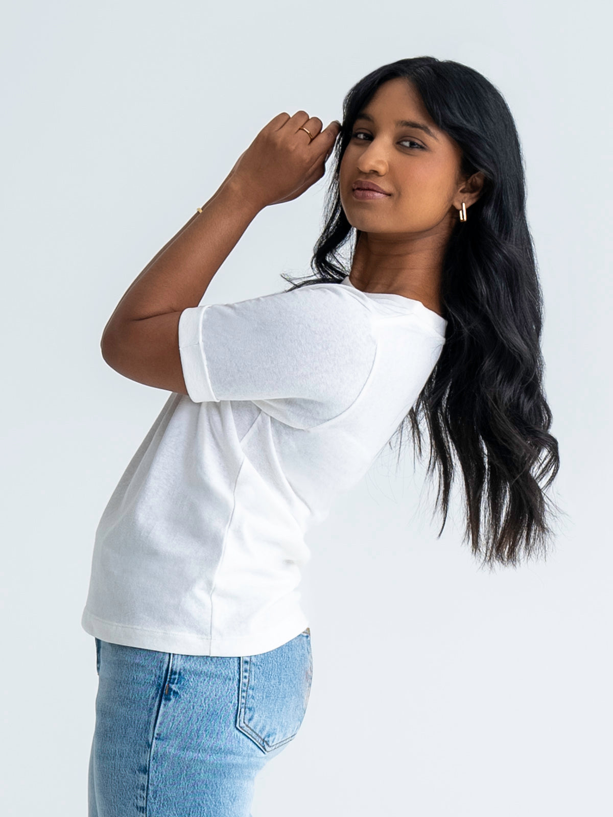 Side view of relaxed fit t-shirt in white, shown untucked, worn with jeans. T-shirt finishes mid-hip. Model wears size 8.